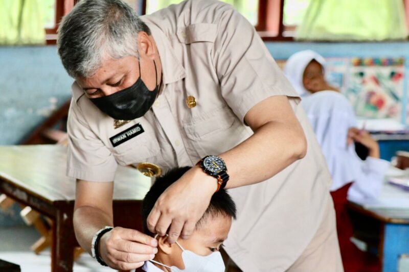 Bupati Pinrang Irwan Hamid Memasangkan masker kepada seorang peserta didik untuk mematuhi protokol kesehatan